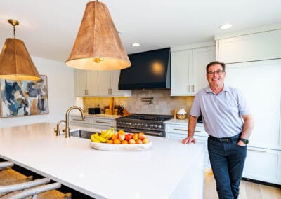 A man stands in a modern kitchen, featuring a spacious island at the center, surrounded by sleek cabinetry and appliances.
